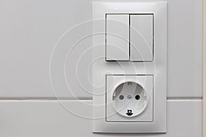 Close up view of white light swithch and socket pair on white tile. Building construction elements concept. Interior.