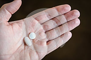 A white male hand holding two white pills in the palm against a dark background