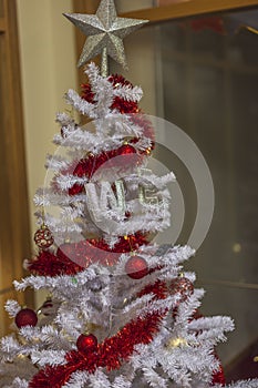 Close up view of white plastic Christmas tree decorated with red tinsel and christmas balls.