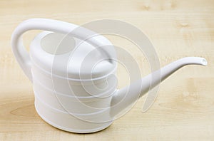 Close up view of white watering can for watering flowers isolated on wooden background.