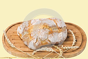 Close up  view of whole grain loaf white bread and wheat ears on a cutting board isolated on yellow background