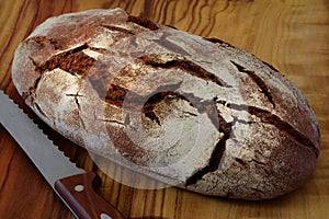 Whole loaf of a country bread on a wooden cutting board with a k