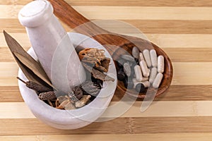Close-up view of whole spices for grinding in mortar pestle with herbal capsules and tablets in a wooden spoon on a chopping board