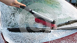 Close up view of windshield covered with snow which is cleaned by man with brush