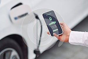 Close up view. Woman charging her electric car and monitoring process on smartphone