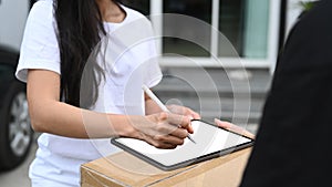 Close up view woman customer signing on digital tablet and receiving package from delivery man.