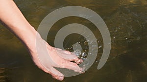 Close up view on woman hand gently touches the surface of the river water. Woman hand runs fingers through water. Slow