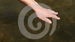 Close up view on woman hand gently touches the surface of the river water. Woman hand runs fingers through water. Slow