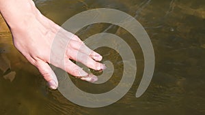 Close up view on woman hand gently touches the surface of the river water. Woman hand runs fingers through water. Slow