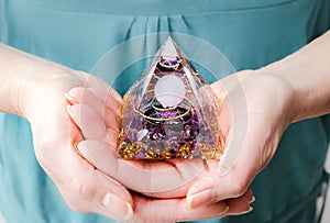 Close up view of woman hands holding and using Orgonite or Orgone pyramid at home while meditating.