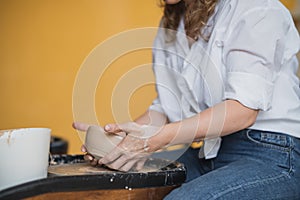 Close-up view of woman hands working on pottery wheel and making clay pot. Hands sculpts a cup from clay pot. Workshop