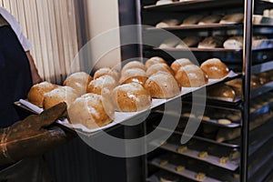 Close up view of woman holding holding rack of rolls in a bakery