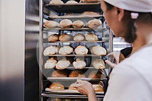 Close up view of woman holding holding rack of rolls in a bakery