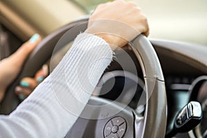 Close up view of woman holding steering wheel driving a car on city street on sunny day