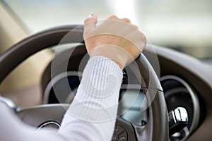 Close up view of woman holding steering wheel driving a car on city street on sunny day