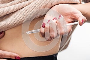 Close up view of woman making injection in stomach with syringe isolated