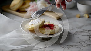 Close up view of a woman putting clotted cream and jam on scone