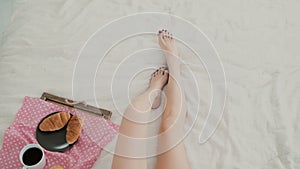 Close-up view of woman s foot. Young girl lying on the bed, having breakfast in living room.