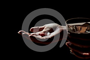 Close-up view of woman`s or girl`s hand holding medication pills, tablets and glass of water. Night photo with high contrast,