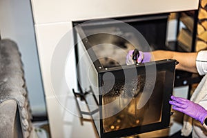 Close-up view of woman\'s hand cleaning soot from glass door of fireplace using spray.