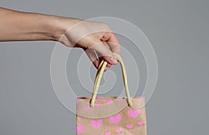 Close up view of a woman`s hand holding a pink gift  bag  on a gray background . Valentine`s day gifts
