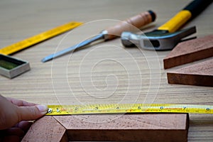 Close up view of a woman`s hands measuring wooden plank with a Tape measure with a set collection of working hand tools