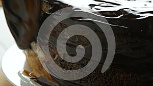 Close up view. Woman spreading a hocolate glaze on a sponge cake. Female hand pour cream with a spoon on the cake and