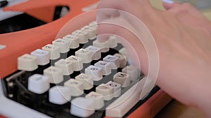 Close up view: woman typing on old vintage orange typewriter on table