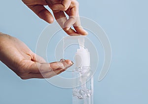 Close up view of woman using hand sanitizer dispenser, blue clean minimalist background. Health concerns concept.