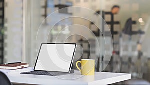 Close up view of workplace with blank screen tablet, office supplies  and coffee cup on white table with blurred  office room