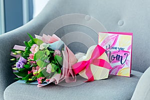 close up view of wrapped bouquet of flowers, heart shaped gift and i love you mom postcard on armchair, mothers