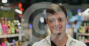 Close up view of young cheerful man looking to camera while walking at soft drink section. Portrait of happy millennial