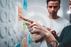 Close-up view of young colleagues hands while posted project plan on note sticky on glass wall in smart office