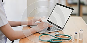 Close-up view of young female doctor examining the patient chart while using mock up laptop computer