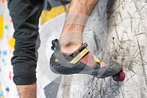 Close up view of young man or climber feet in climbing shoes on artificial indoor wall at climbing center, sport