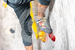 Close up view of young man or climber feet in climbing shoes on artificial indoor wall at climbing center, sport