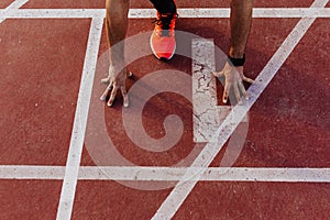 Close up view of young muscular athlete is at the start of the race tracks line at the stadium. Sports concept