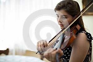 Close-up view of a young woman playing the violin in the privacy of her home.