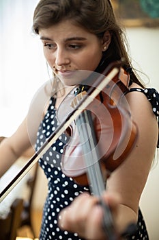 Close-up view of a young woman playing the violin in the privacy of her home.