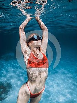 Close up view of young woman in red bikini underwater in blue ocean. Beautiful lady freediver float up to ocean surface