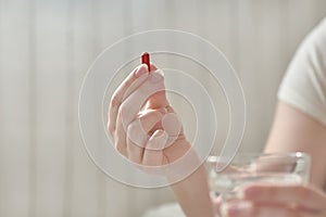 Close-up view of young woman`s hands. Girl in bed holding tablets or pills and glass of water. Blurred background