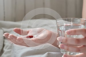 Close-up view of young woman`s hands. Girl in bed holding tablets or pills and glass of water. Painkiller with space for text