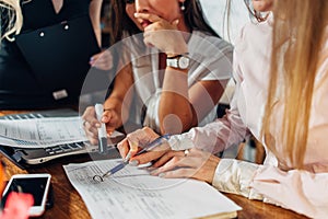 Close-up view of young women working on accounting paperwork checking and pointing at documents sitting at desk in