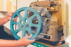Close up of vintage classic mobile 8 mm or 16 mm movie film projector and hand holding empty film reel with vintage color style.