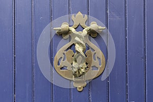 Close-up. Vintage handle for knocking on a blue wooden door in the form of two wriggling snakes