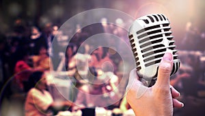 Close up vintage microphone in singer hand singing on stage of wedding event party or business meeting with lighting effect and co