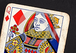 Close up of a vintage queen of diamonds playing card on a black background.