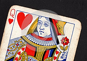 Close up of a vintage queen of hearts playing card on a black background.