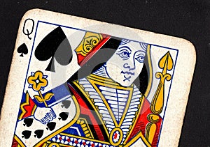 Close up of a vintage queen of spades playing card on a black background.