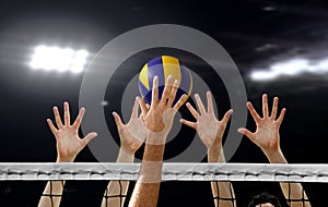 Close up of Volleyball spiking and hand blocking over the net under bright spotlights